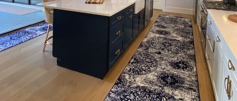 A modern kitchen with a central island, pendant lights, and a patterned rug.
