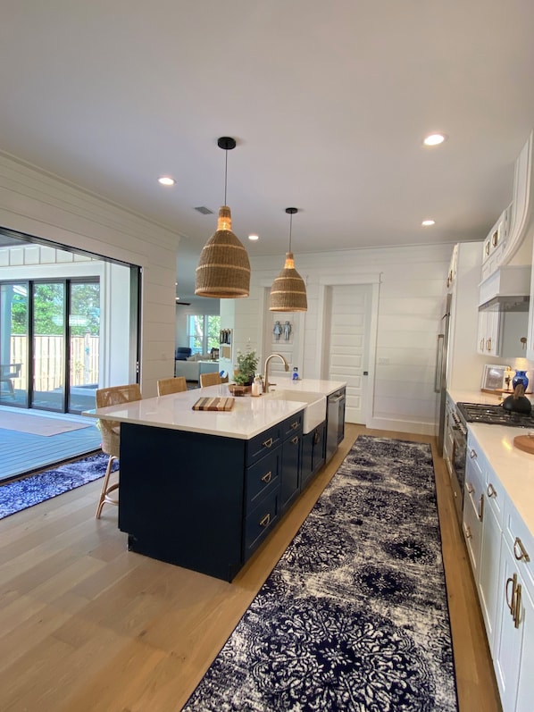 A modern kitchen with a central island, pendant lights, and a patterned rug.