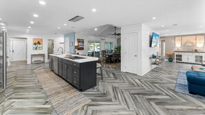 Una cocina moderna con una isla central, un comedor con una mesa grande y una sala de estar con un sofá azul.