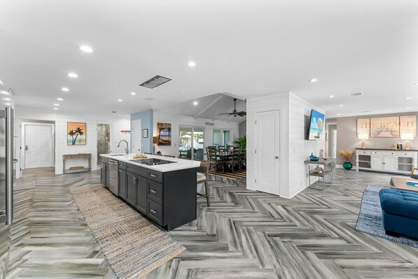 A modern kitchen with a central island, a dining area with a large table, and a living room with a blue sofa.
