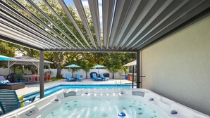 Un jacuzzi con una pérgola, una piscina y sillas de descanso.