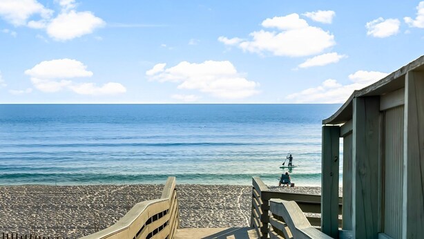 Una terraza de madera que da a una playa con vistas despejadas al océano y una persona en el agua.