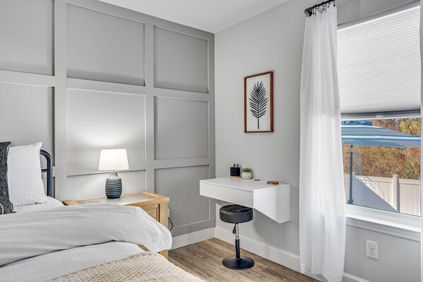 A bedroom with a bed, bedside table, lamp, and a small white shelf with decorative items.