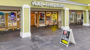 Un área de estar al aire libre con mesas y sillas frente a un edificio llamado 'AXE THROWING'.