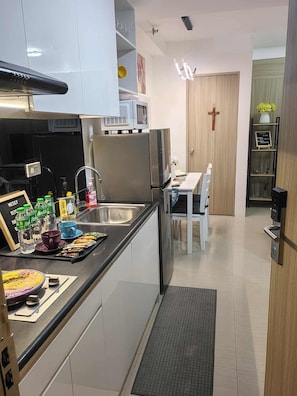 A modern kitchen with a built-in microwave, stainless steel appliances, a sink, and a dining area with a white table and chairs. - Private place 2 BR with Balcony located in prime location in mall of Asia (Pasay)