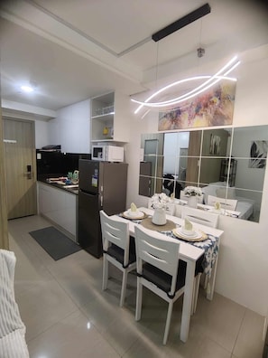 A modern kitchen with white cabinetry, a refrigerator, a microwave, and a dining area with white chairs and a table set for two. - Private place 2 BR with Balcony located in prime location in mall of Asia (Pasay)