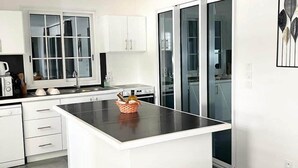A modern kitchen with white cabinetry, a central island, and a glass door leading to a dining area. - Le Roc de Malendure (Bouillante)