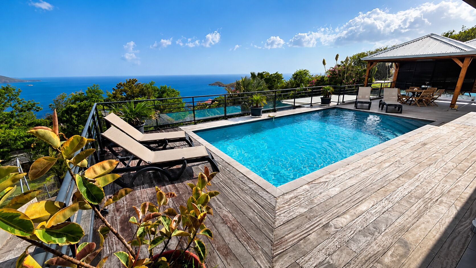 A pool with a wooden deck and lounge chairs, overlooking a body of water.