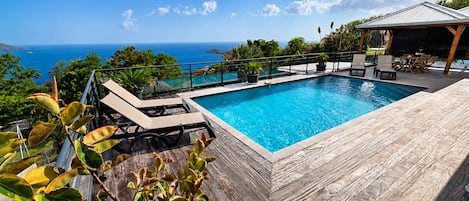 A pool with a wooden deck and lounge chairs, overlooking a body of water.