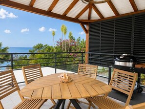 An outdoor patio with a round wooden table, chairs, and a grill.