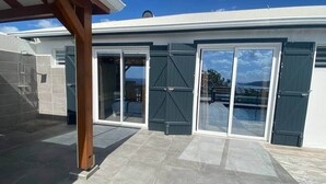 A modern house with a covered patio, large sliding glass doors, and a swimming pool in the background. - Le Roc de Malendure (Bouillante)