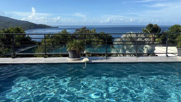 A swimming pool with a view of the ocean and a mountainous landscape. - Le Roc de Malendure (Bouillante)