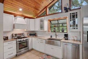 A modern kitchen with white cabinets, stainless steel appliances, and a large window with decorative items. - River House with Dock, Waterfront Stunner Sunrise to Sunset (St Johns)