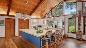 Un'ampia cucina con una grande isola, soffitto in legno e ampie finestre con vista sull'esterno.