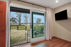 A room with a sliding glass door leading to an outdoor deck, a flat-screen TV mounted on the wall, and a wooden floor.