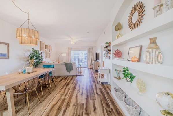 Una sala de estar moderna con una mesa de comedor de madera, sillas traslúcidas, un sofá y un ventilador de techo.