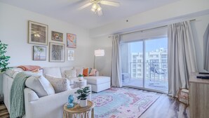 A modern living room with a white sofa, a coffee table, and a large window with a view of buildings.