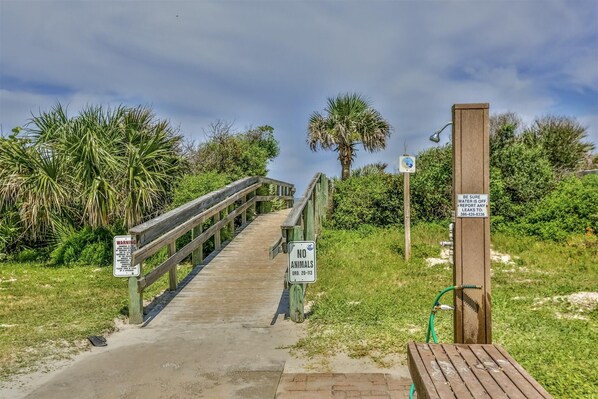 A wooden boardwalk leading to a beach area with signs indicating no animals allowed and a warning about water being off.