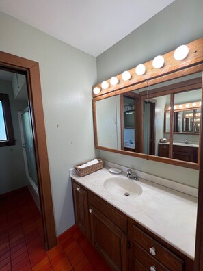 A bathroom with a vanity, a mirror with lights, a sink, and a wooden cabinet.