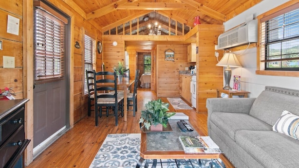 A cozy cabin interior with a dining area, a living room with a sofa, and a kitchen area.