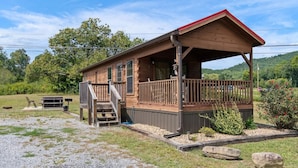 A wooden cabin with a porch, a picnic table, and a grill area.