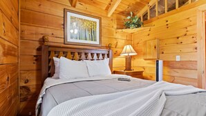 Una camera da chalet in legno con un letto, una cornice con un'immagine appesa al muro, un comodino con una lampada e una piccola pianta su una mensola.