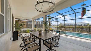 A spacious patio with a dining table and chairs, a hanging wind chime, and a view of a swimming pool. - Spacious 6-bedroom 5.5 baths Sleeps 16 with a Private Heated Pool/Spa (Davenport)