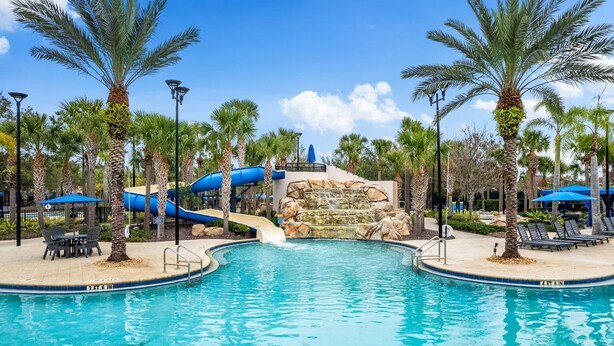 A pool area with a water slide, palm trees, and lounge chairs. - Spacious 6-bedroom 5.5 baths Sleeps 16 with a Private Heated Pool/Spa (Davenport)