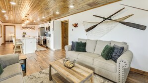 A spacious living area with a wooden ceiling, a sofa with decorative pillows, a coffee table, and a kitchen in the background. - Riverfront Home w/ Private Dock in Wisconsin Dells (Wisconsin Dells)