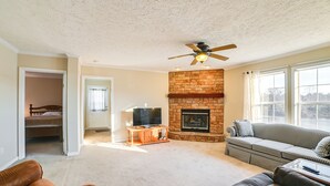Una sala de estar con chimenea, ventilador de techo y un ventanal grande.