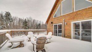 Una terraza de madera con sillas y una mesa cubiertas de nieve, con vistas a un paisaje nevado.