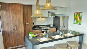 A modern kitchen with a central island, pendant lights, and a refrigerator. - A Peaceful, Tropical Loft in the heart of the Riviera Maya (TLM Akumal)