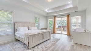 A bedroom with a large bed, a nightstand, a dresser, and a view of the outdoors through a sliding glass door. - Waterfront Retreat w/ Outdoor Oasis in Pensacola (Pensacola)
