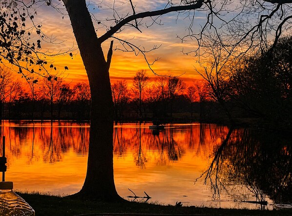 A serene sunset over a calm lake with trees silhouetted against the sky. - Relaxing Lake House Retreat on 12 Acres (Texarkana)