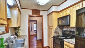 A kitchen with wooden cabinets, a granite countertop, a stainless steel sink, a black stove, and a microwave.