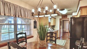 A dining area with a round wooden table, chairs, a potted plant, and a kitchen in the background.