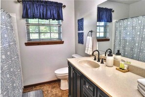 A bathroom with a sink, toilet, and window with curtains. - Relaxing Lake House Retreat on 12 Acres (Texarkana)