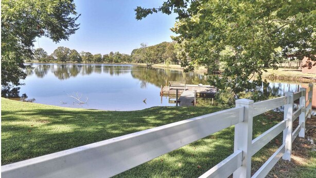 A serene lakeside view with a wooden dock and a white fence.