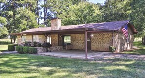 A brick building with a covered patio, a flag, and a chimney. - Relaxing Lake House Retreat on 12 Acres (Texarkana)