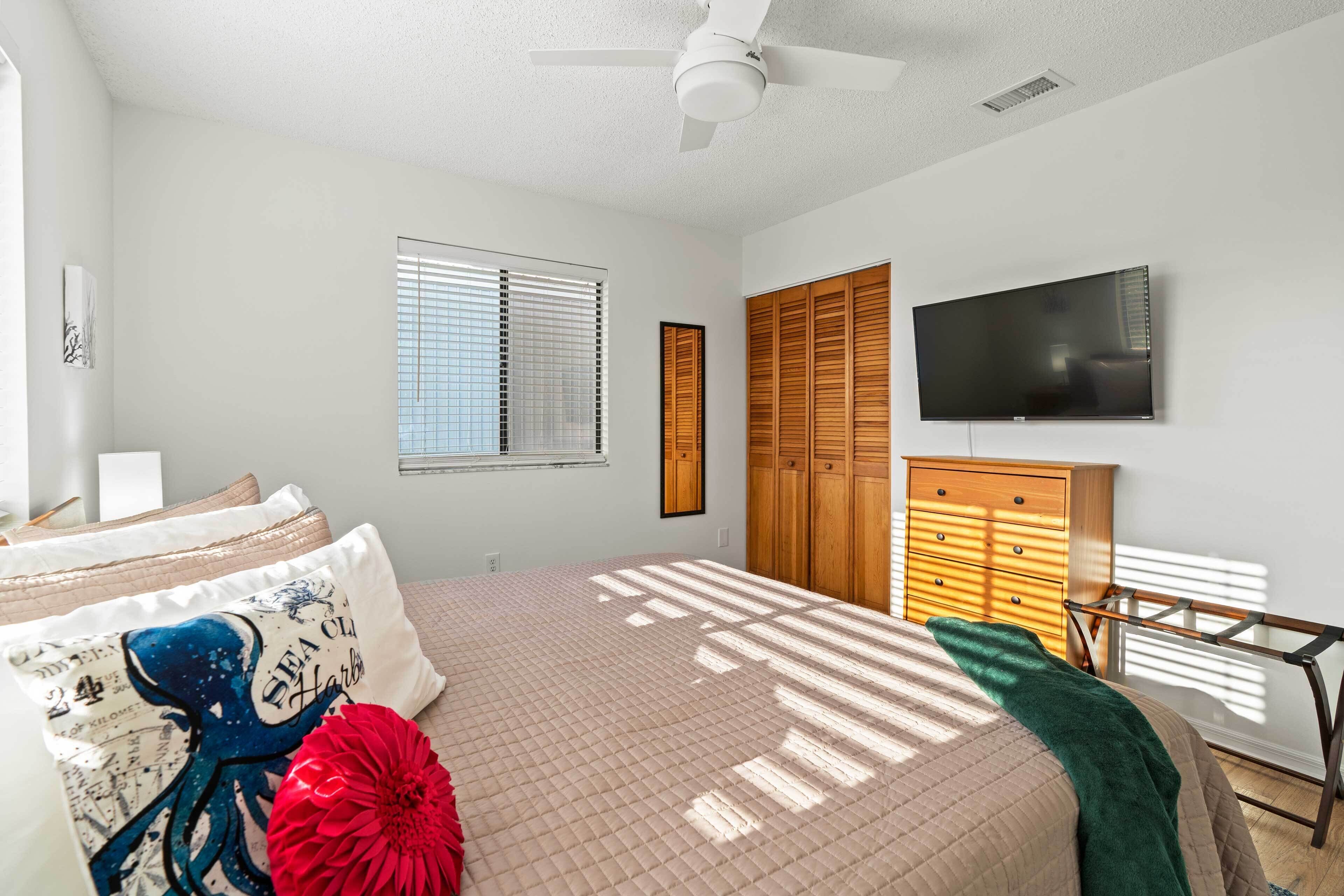 A bedroom with a bed, a TV, wooden cabinets, and a ceiling fan.
