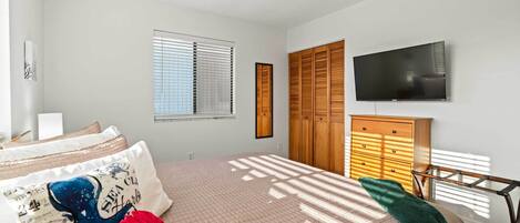 A bedroom with a bed, a TV, wooden cabinets, and a ceiling fan.