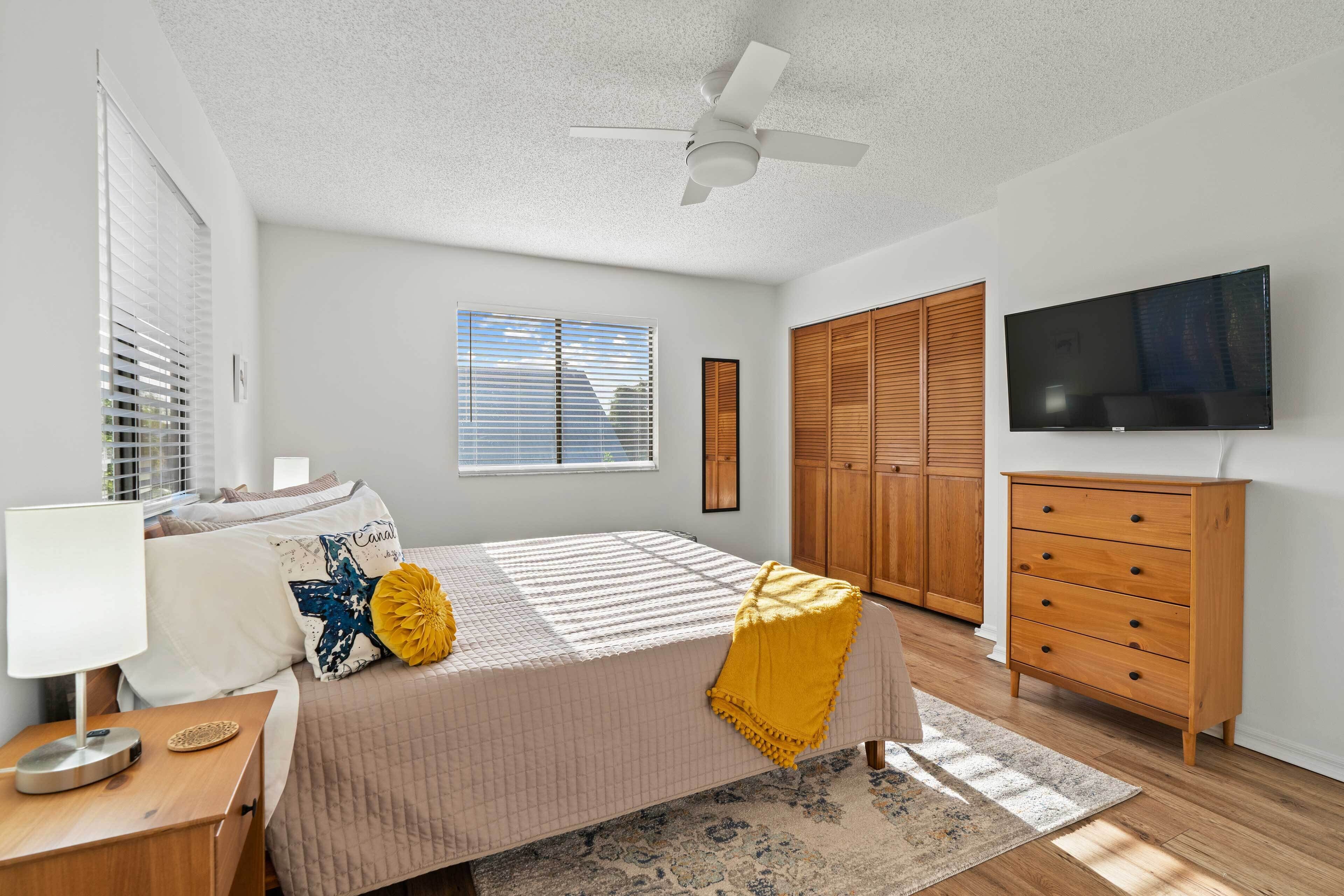 A bedroom with a bed, a nightstand, a dresser, a television, and a ceiling fan.