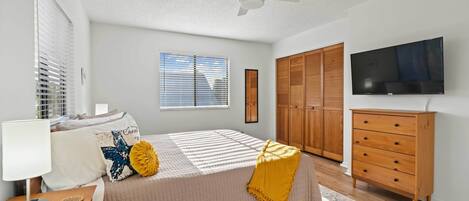 A bedroom with a bed, a nightstand, a dresser, a television, and a ceiling fan.