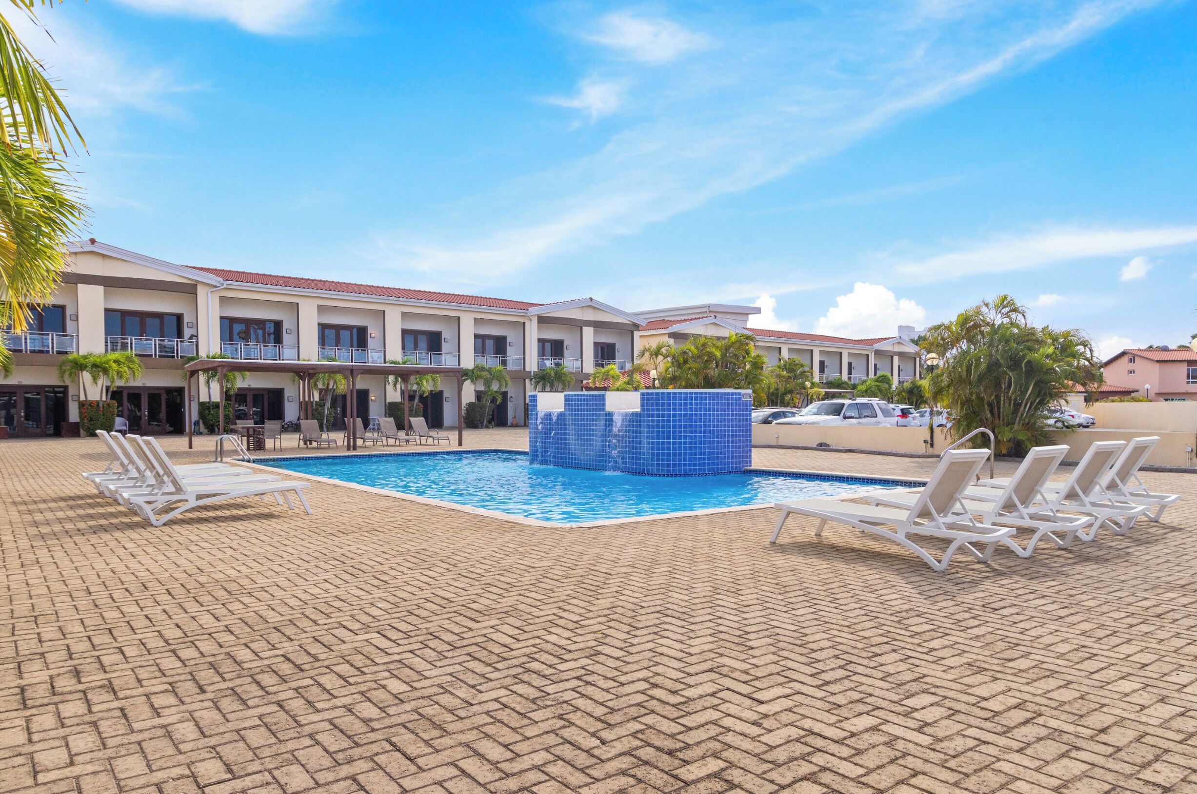A hotel pool area with lounge chairs, a blue water feature, and a clear sky.