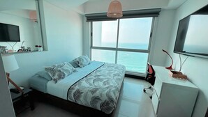 Un dormitorio moderno con una cama grande, televisión y vistas al mar.
