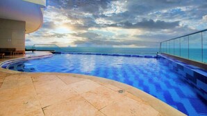 Una piscina con borde curvo, vista despejada del océano y cielo nublado.
