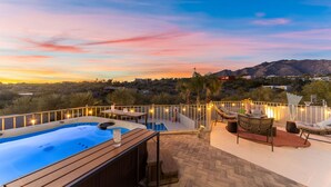 Eine Dachterrasse mit Whirlpool, Sitzgelegenheiten im Freien und Blick auf eine Berglandschaft bei Sonnenuntergang.