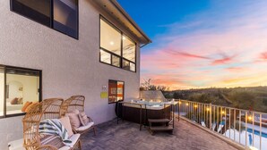 Eine Terrasse mit Korbmöbeln, einem Whirlpool und Blick auf einen Pool bei Sonnenuntergang.
