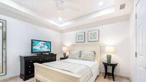 Une chambre à coucher avec un lit, une télévision, deux tables de chevet avec des lampes et des tableaux encadrés accrochés au mur.