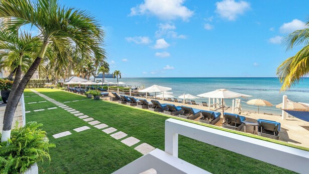 Une pelouse bien entretenue, avec un chemin menant à une zone de plage équipée de chaises longues et de parasols.